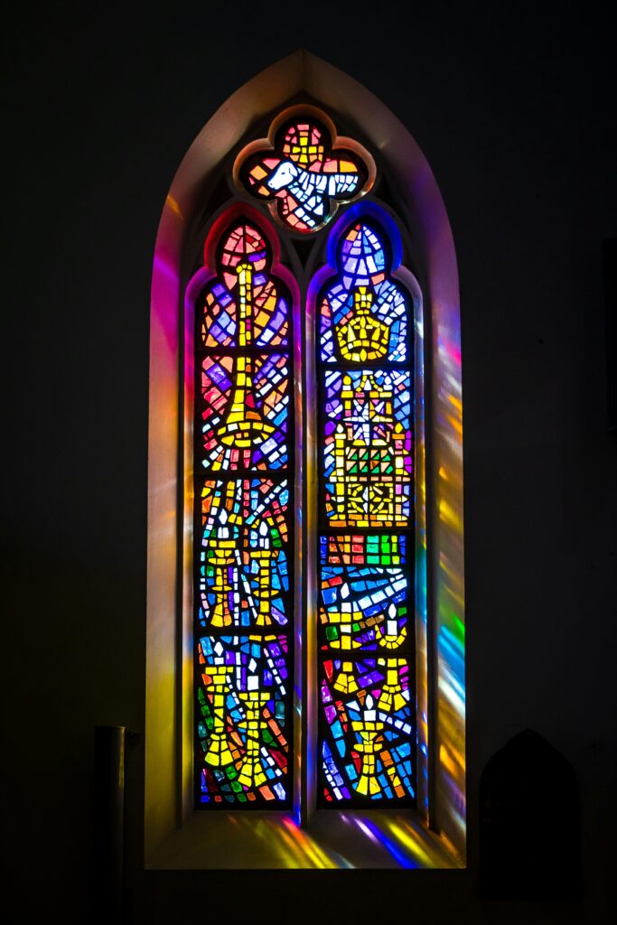 Colorful stained glass window in a church captured at dawn with vibrant light reflections.