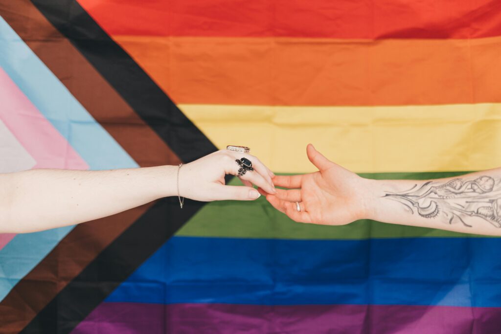 Connected hands in front of a progress pride flag, symbolizing unity and support within the LGBTQ+ community.